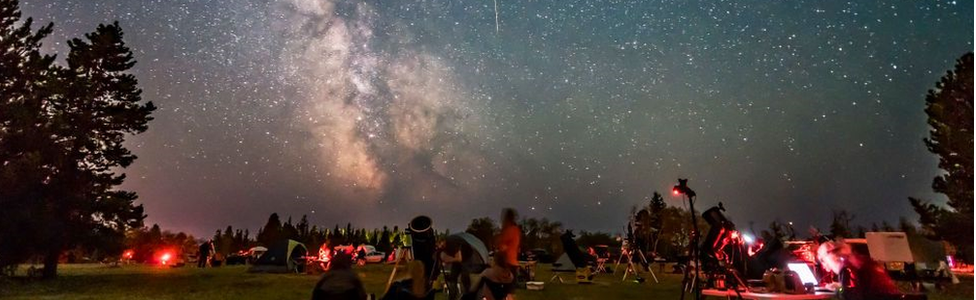 A group of people stargazing, the sky is lit with meteorites and the milky way