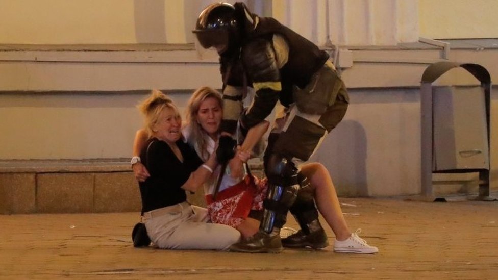Izbori u Belorusiji: Policija koristila bojevu municiju u sukobu sa demonstrantima, napadnuta BBC ekipa 1 A riot police officer tries to move two women sitting on the pavement in Minsk, Belarus. Photo: 10 August 2020