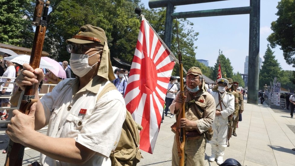 People wearing Japanese Imperial army and navy costumes hold a rising sun flag as they pay tribute to the war dead at Yasukuni Shrine