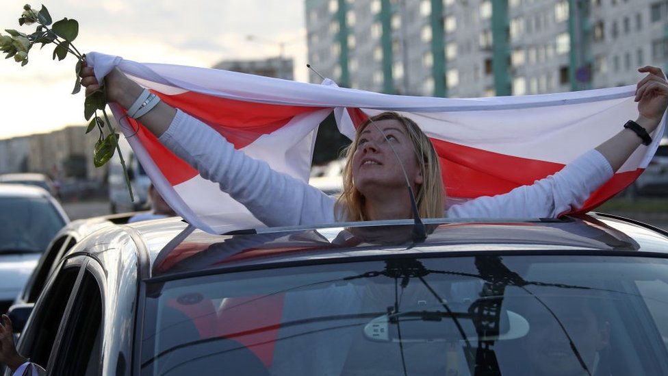 Izbori u Belorusiji: Talas štrajkova posle masovnih protesta na kojima se zahteva ostavkapredsednika Aleksandra Lukašenka 4 A car passenger displays a Belarusian flag