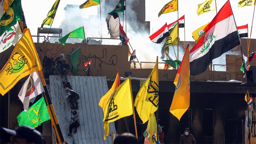 Supports of Iraqi militias climb onto the outer walls of the US embassy in Baghdad during a protest on 1 January 2020