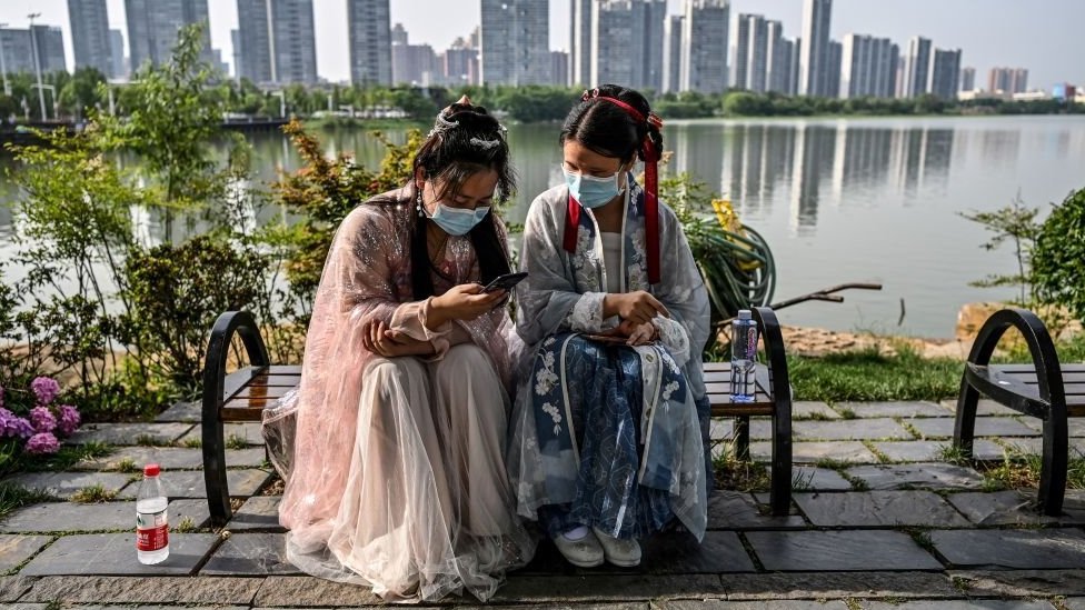 Two Chinese girls dressed in traditional ceremonial clothes look at their phones in the city of Wuhan