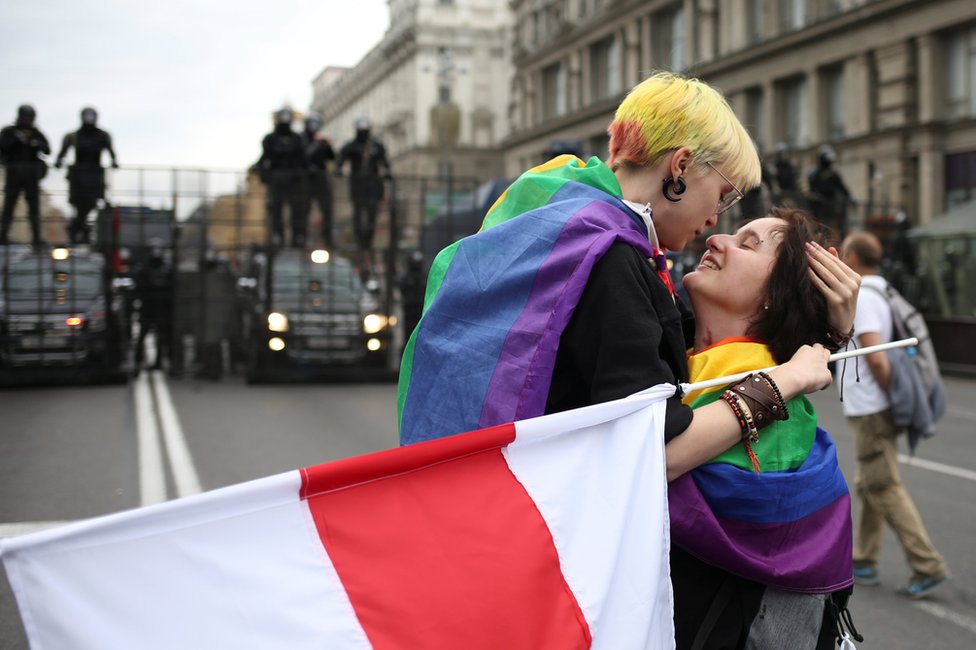 Participants with rainbow-themed flags, representing the LGBT symbol, embrace near barriers erected by Belarusian law enforcement officers during an opposition rally to protest against police brutality and to reject the presidential election results in Minsk, Belarus, 6 September