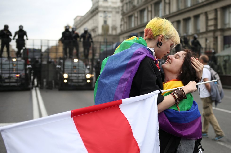 Participants with rainbow-themed flags, representing the LGBT symbol, embrace near barriers erected by Belarusian law enforcement officers during an opposition rally to protest against police brutality and to reject the presidential election results in Minsk, Belarus, 6 September