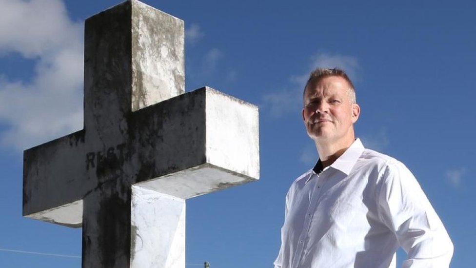 Bill Edgar standing next to a stone cross