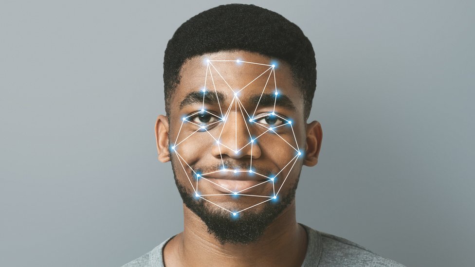A stock image shows a black man smiling at the camera, while a network of lights and dots is superimposed over his face to illustrate the concept of facial recognition