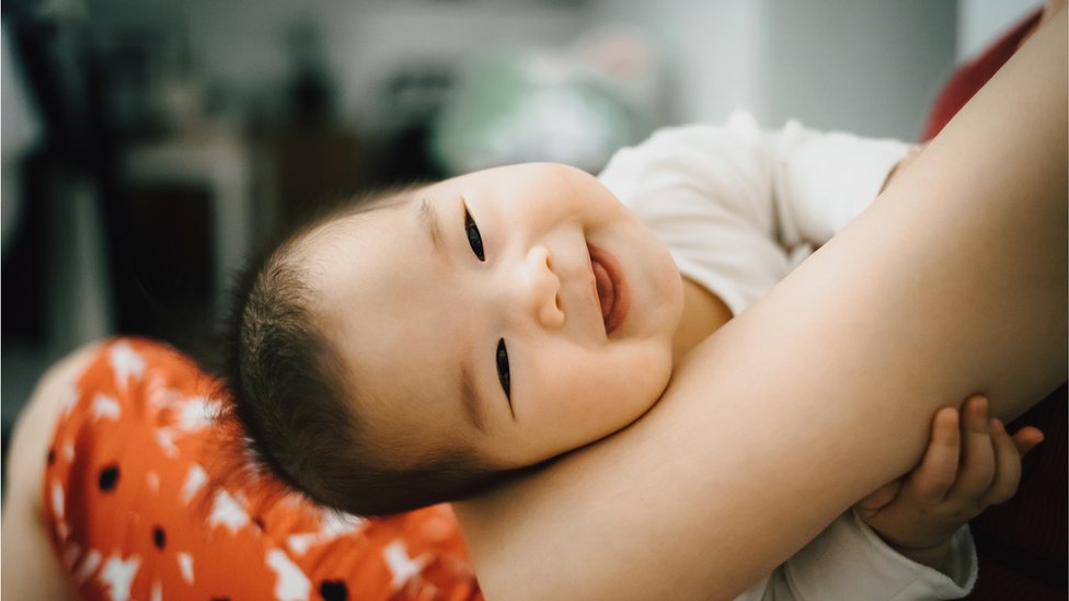 A photo of a smiling baby in mother's arms.