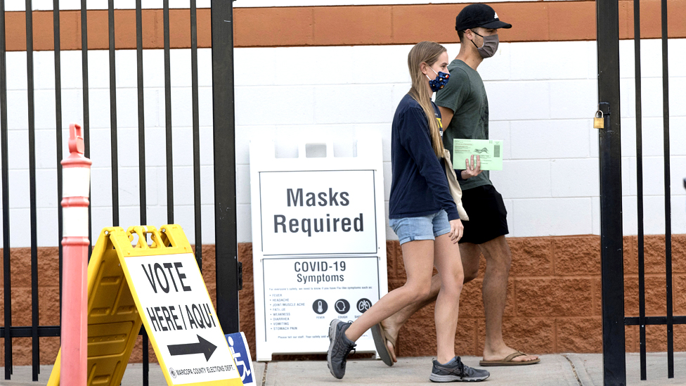 Voters walk to a polling station to deliver their mail-in ballots in green envelopes