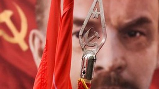 A picture of Vladimir Lenin behind a standard showing the communist symbol