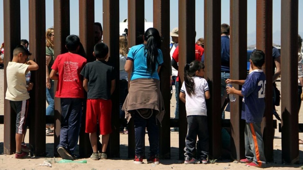 Children look through the US-Mexico border wall