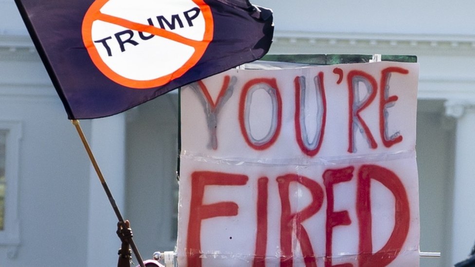 A flag and a "you're fired banner" in front of the White House