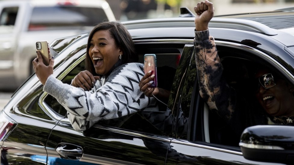 A woman uses her phone as she celebrates from a car