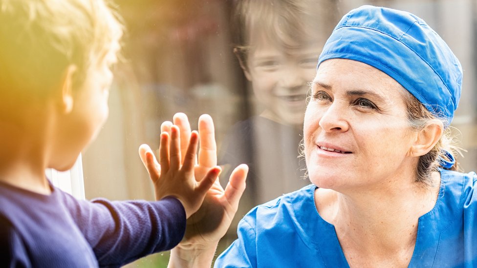Korona virus, psihologija i fizičko distanciranje: Šta se dešava kad ne smemo da dodirujemo jedni druge? 1 A health worker and her son are separated by a window - they both put up their hands to touch through the glass