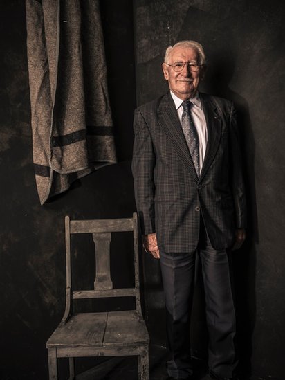 Portrait of Eddie Jaku with a chair and a blanket like the ones he used to have in Auschwitz