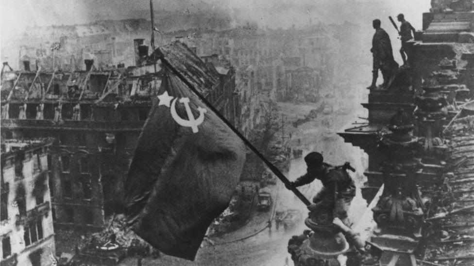 Russian soldiers flying the Red Flag over the ruins of the Reichstag in Berlin.