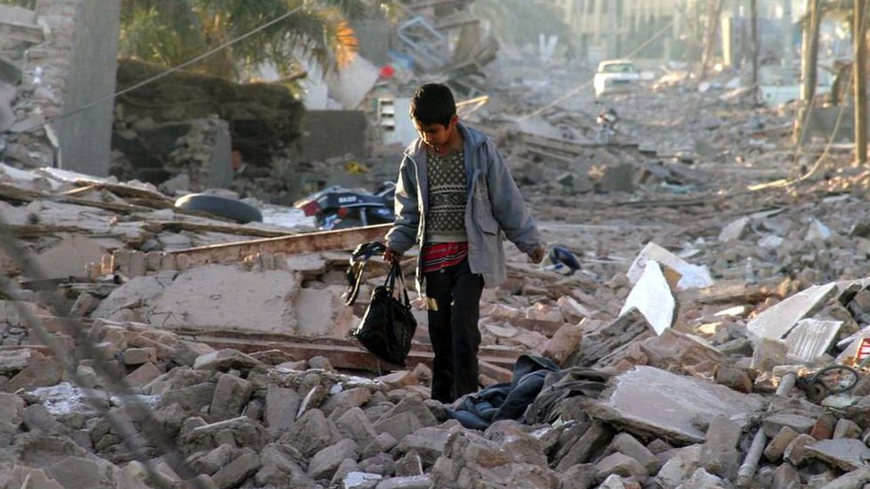 An boy carrying a bag walks on a street where debris is seen after the earthquake in Bam, on 28 December 2003