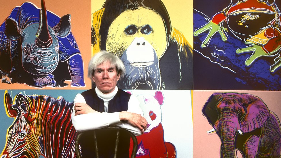 American Pop artist Andy Warhol sits in front of several paintings in his 'Endangered Species' series