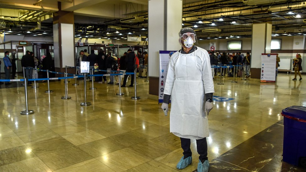 Korona virus, lažni testovi i Avganistan: Na šta su sve ljudi spremni samo da putuju 6 A health services staff member wearing protective gear looks on as he waits to check