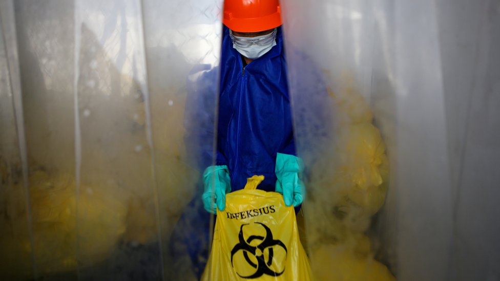 Person in PPE holding a bag of medical waste