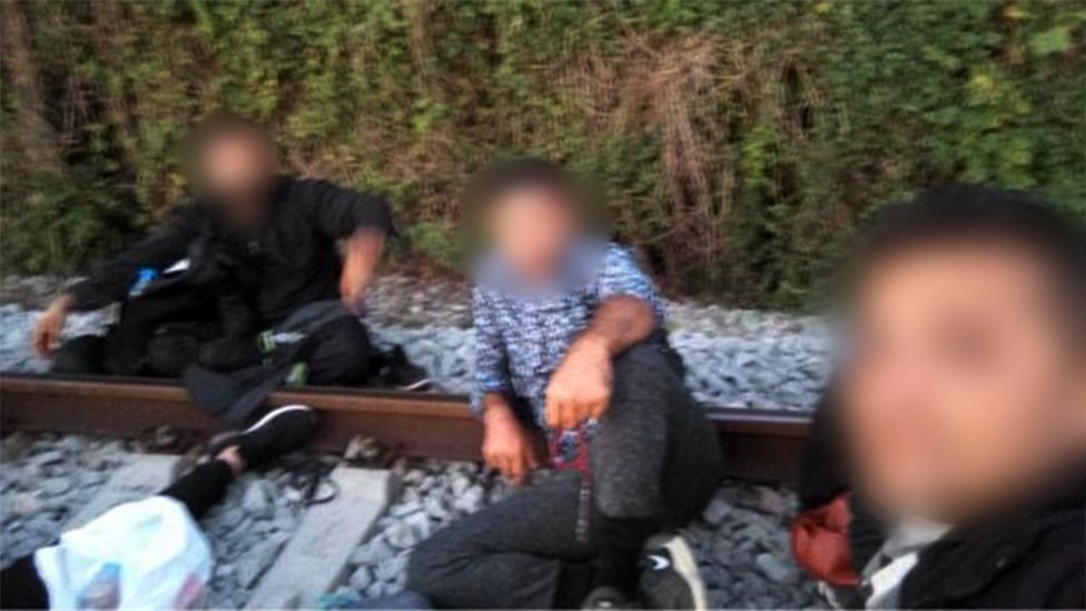 Three migrants pose in a selfie on some railtracks (faces are obscured to prevent identification)