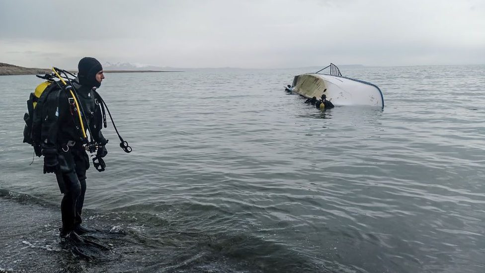 A diver looks at colleagues in the water by an overturned boat