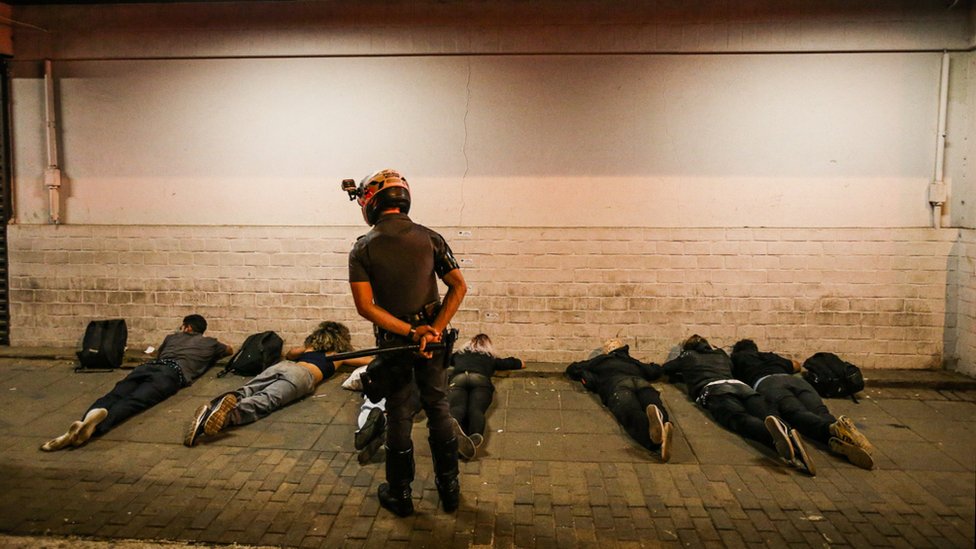 Seven BLM protesters lie on the ground as a policeman stands over them
