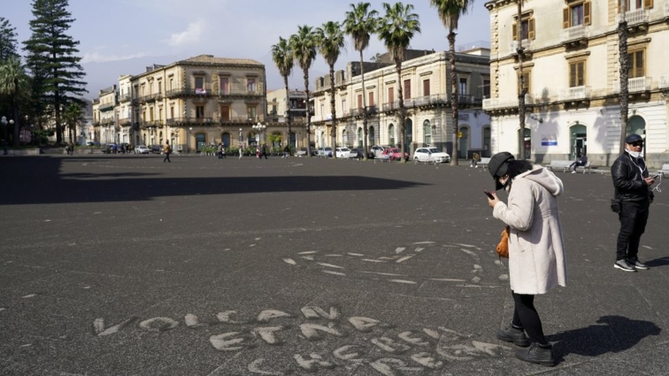 Italija i vulkan Etna: Život ispod diva koji se stalno budi i preti 8 A person stands next to a sign made with ashes from Mount Etna that reads "Etna volcano what a nice gift" in Giarre, Italy, February 28, 2021