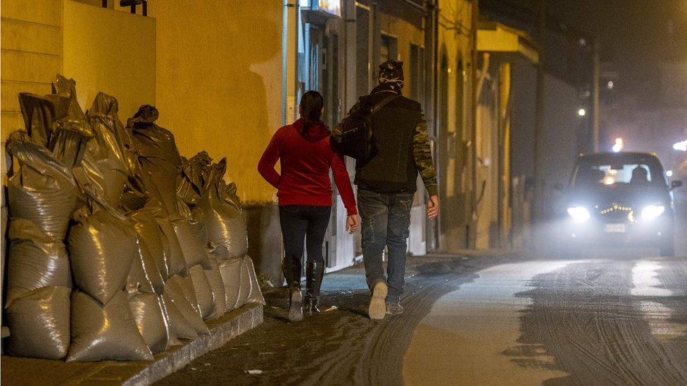 Residents walk on ashes, past bags filled with ashes from the Mount Etna volcano stored aside after being swept by municipal employees from a street of Zafferana Etnea, north of Catania,