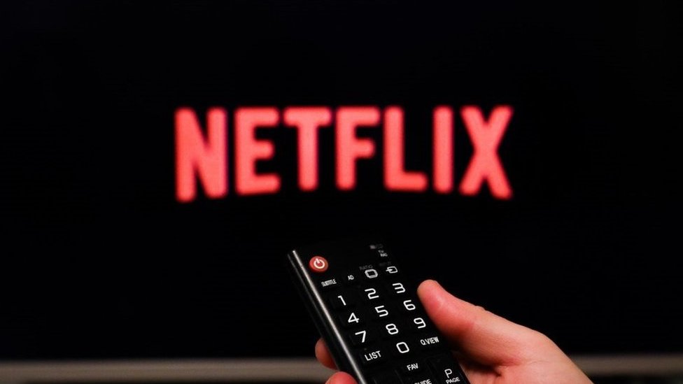 Netflix logo on a TV with hand holding remote