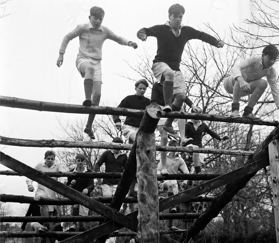A black and white picture of pupils at Gordonstoun School doing physical training on an obstacle course in 1956