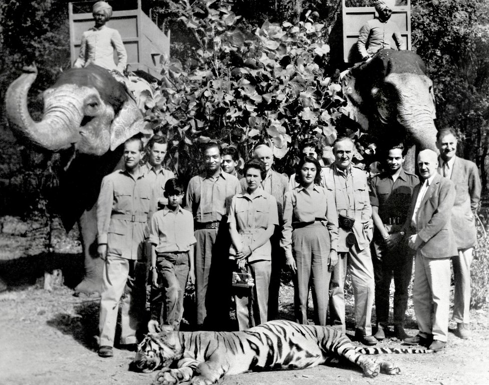A black and white picture from 1961 shows the Queen, Prince Philip, the Maharaja and Maharani of Jaipur, India, and several others, standing in front of a tiger he had killed