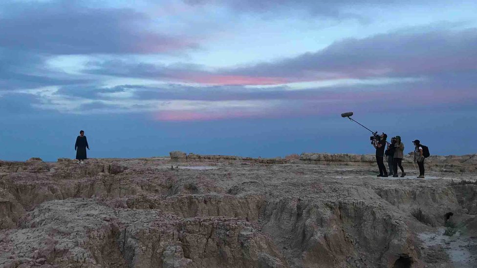 A film crew film a women in a barren landscape
