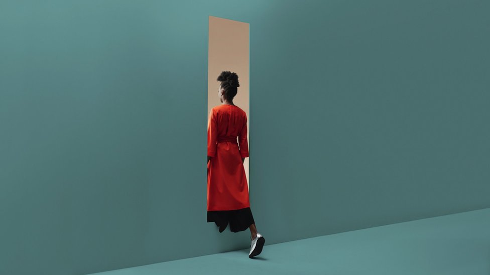 Concept image: woman in a red dress walking through a gap in a blue wall
