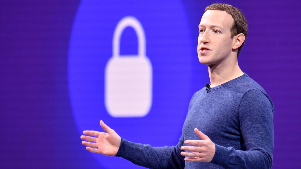 Mark Zuckerberg gestures with arms open in front of a padlock symbol on stage during a privacy speech