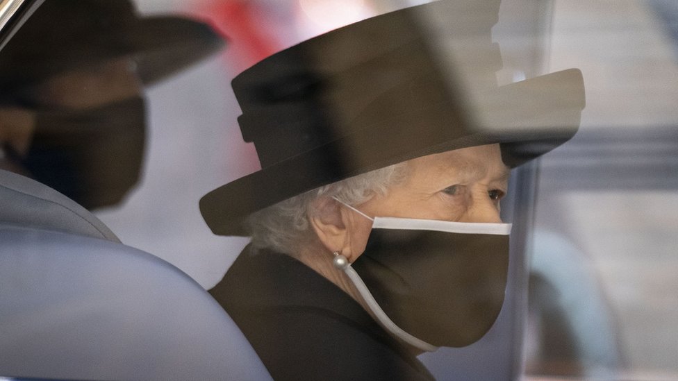 The Queen dressed in black with a black face mask