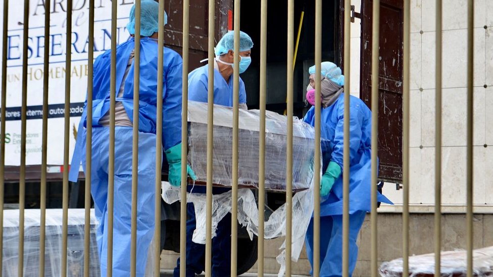 Morgue workers in Ecuador carrying a coffin wrapped up in plastic due to Covid-19