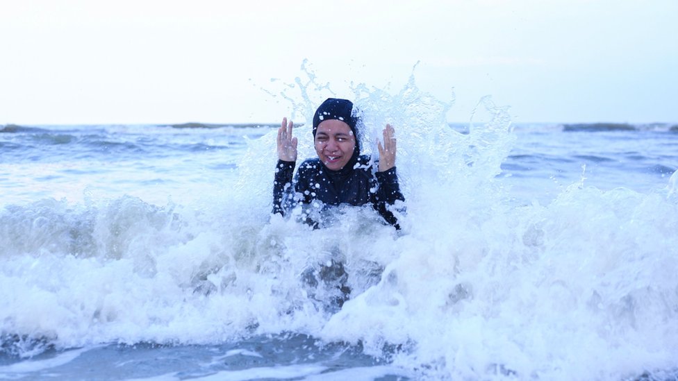 A female Muslim swimmer hit by waves while swimming in the sea.