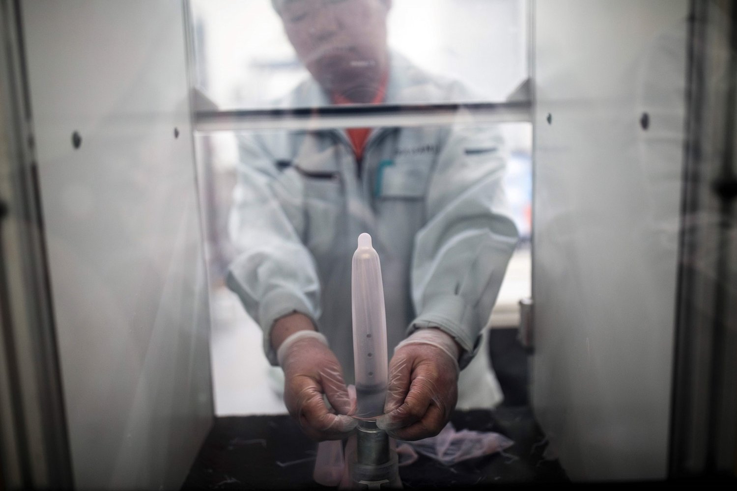 An employee of Japanese condom maker Sagami Rubber Industries puts a condom in a machine to test its endurance by filling it with air