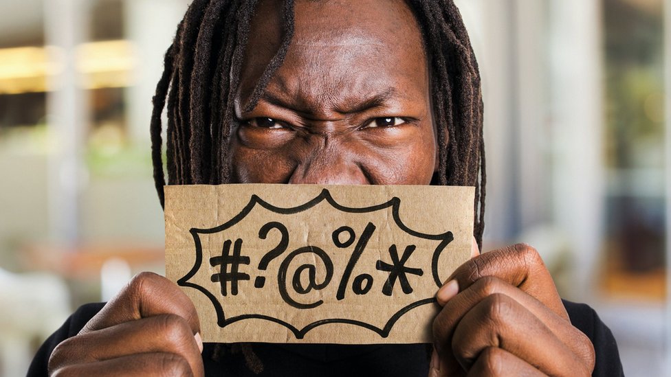 Psihologija i zdravlje: Zašto se osećamo dobro kad psujemo 4 Man holding a small board in front of his mouth, with symbols meaning swear words