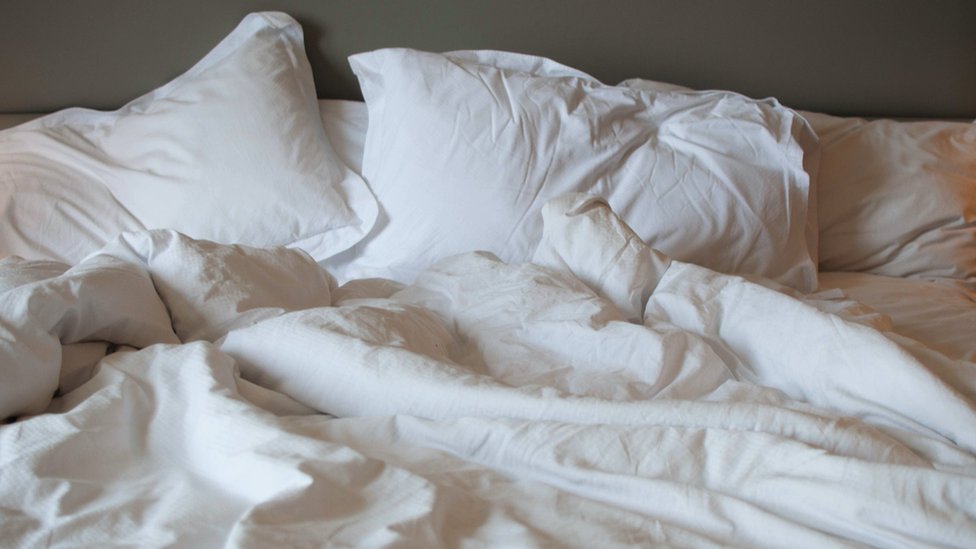 Close-up view of messy bed, with rumpled white linen sheets and big pillows.