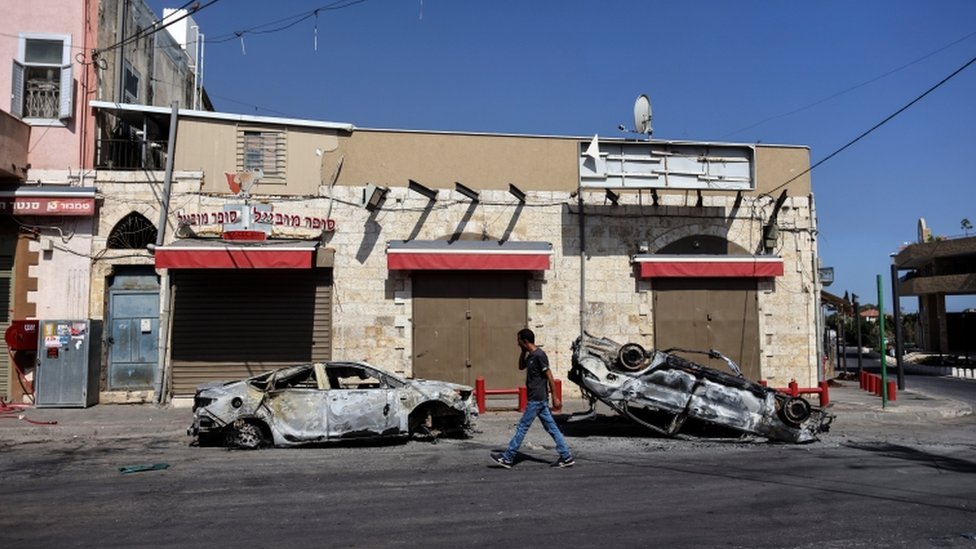 A man walks past two cars burnt during unrest in the Israeli city of Lod