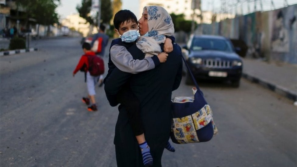 A Palestinian woman carrying her son evacuates after their tower building was hit by Israeli airstrikes, amid a flare-up of Israeli-Palestinian violence, in Gaza City May 12, 2021.