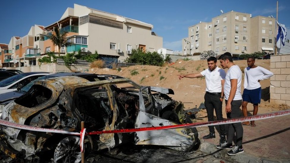 People look at a damaged car at a site where a rocket fired from Gaza landed, as Israeli-Palestinian cross-border violence continues, in Ashkelon, southern Israel, May 16, 2021