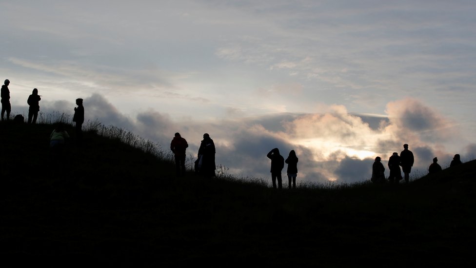 People look at the sunrise during the celebrations of the Summer Solstice, despite official events being cancelled amid the spread of coronavirus, in Avebury