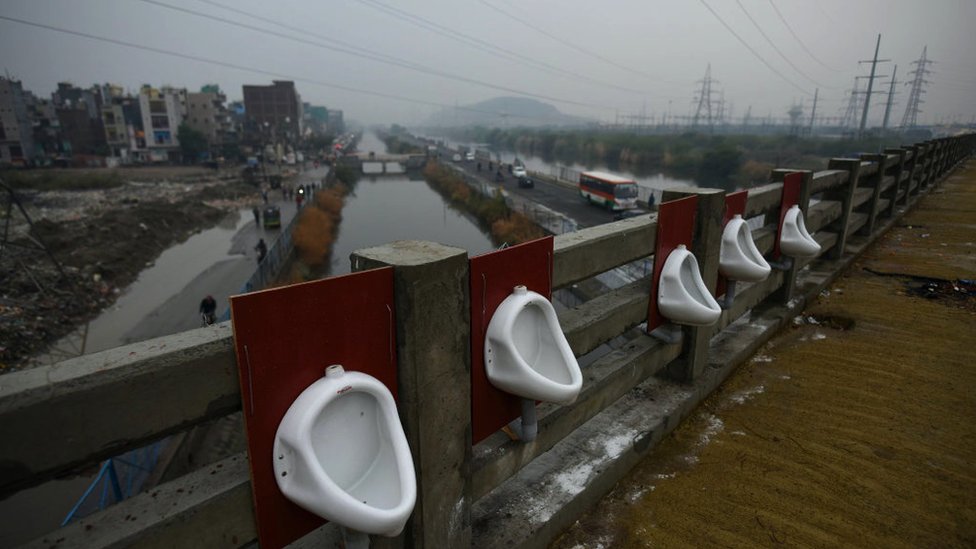 A row of open air public urinals, set up on a bridge spanning over a river and a canal