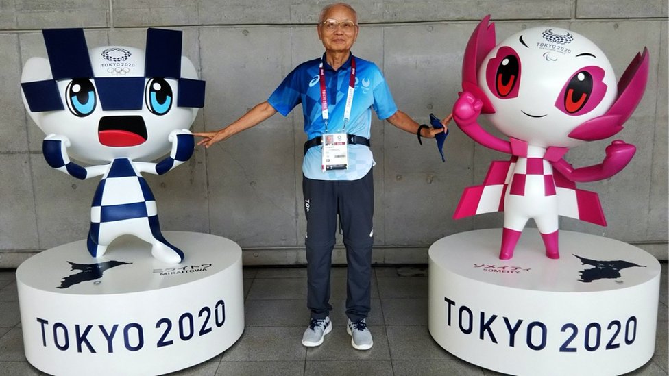 Olimpijske igre u Tokiju: Volonteri na takmičenju drugačijem od svih do sada 3 Katsuya Kato, a 79-year-old volunteer, posing between two Olympics mascots.