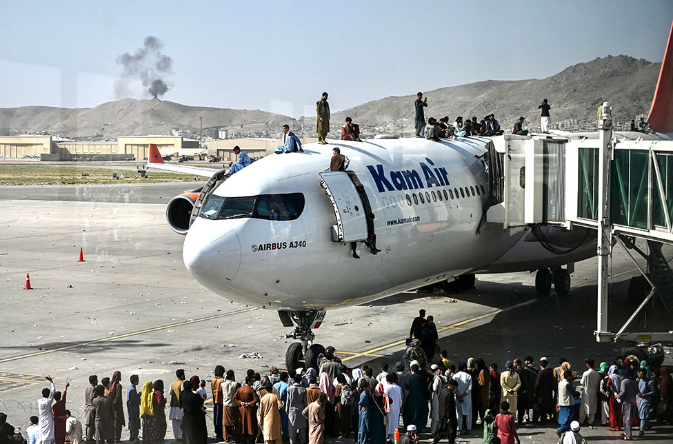 Afghan people climb atop a plane as they wait at the Kabul airport on 16 August 2021