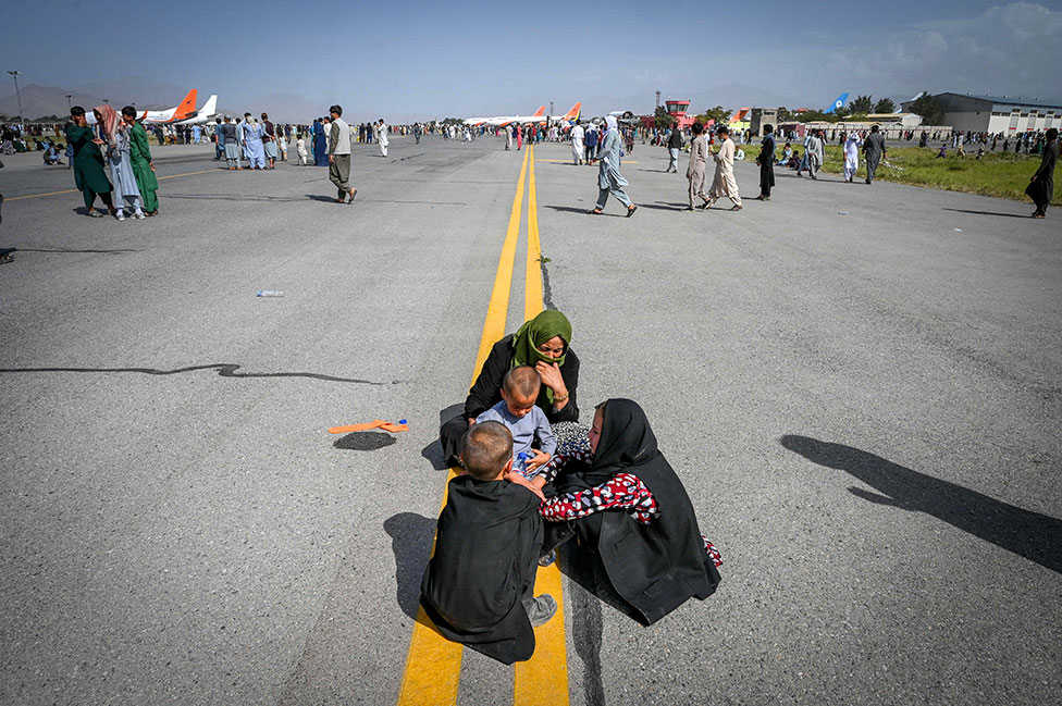 Afghan people sit on the tarmac as they wait to leave the Kabul airport in Kabul on 16 August 2021