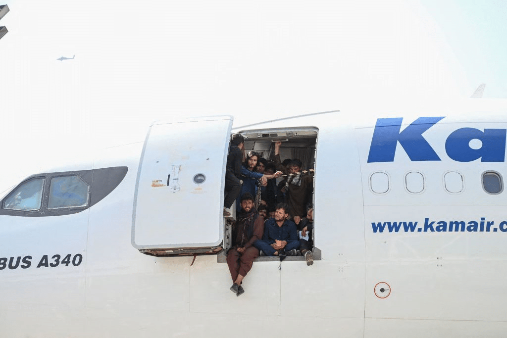 Afghan people climb up on a plane and sit by the door as they wait at the Kabul airport in Kabul on August 16, 2021