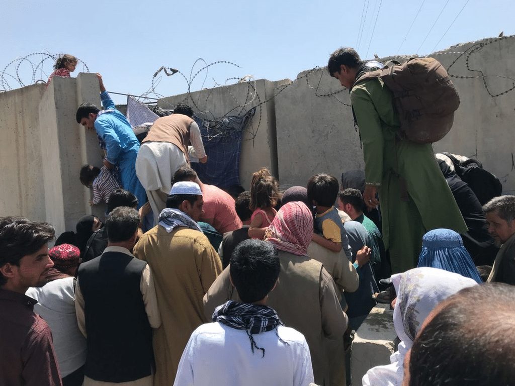 People struggle to cross the boundary wall of Hamid Karzai International Airport